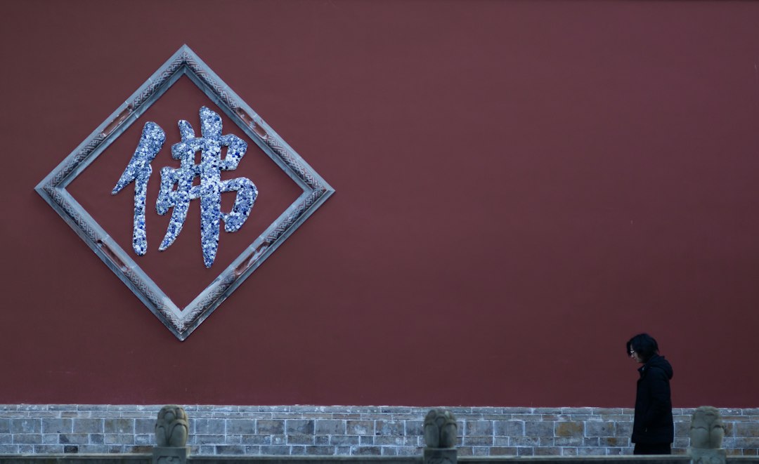 A person walking past a red wall with graffiti on it