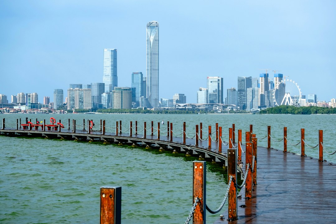 A curved wooden boardwalk over water with the Suzhou skyline in the background