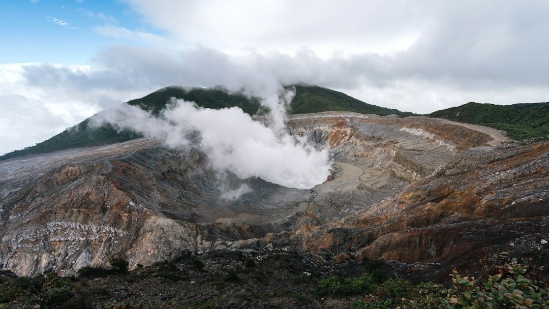 Volcano crater with steam rising under cloudy sky